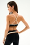 A woman stands sideways wearing the SPLITS59 Scottie Airweight Bra - Black/Creme with matching black leggings featuring white and beige stripes.