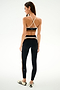 A woman faces away from the camera in SPLITS59 Emerson Airweight High Waist 7/8 - Black/Creme, styled with white sneakers against a plain white background.