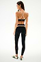A woman faces away against a white background, wearing the SPLITS59 Scottie Airweight Bra - Black/Creme, black striped leggings, and white sneakers with black stripes.