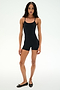 A person wearing the SPLITS59 Airweight 3.5" Short Jumpsuit in black and black ballet flats stands against a plain white background.