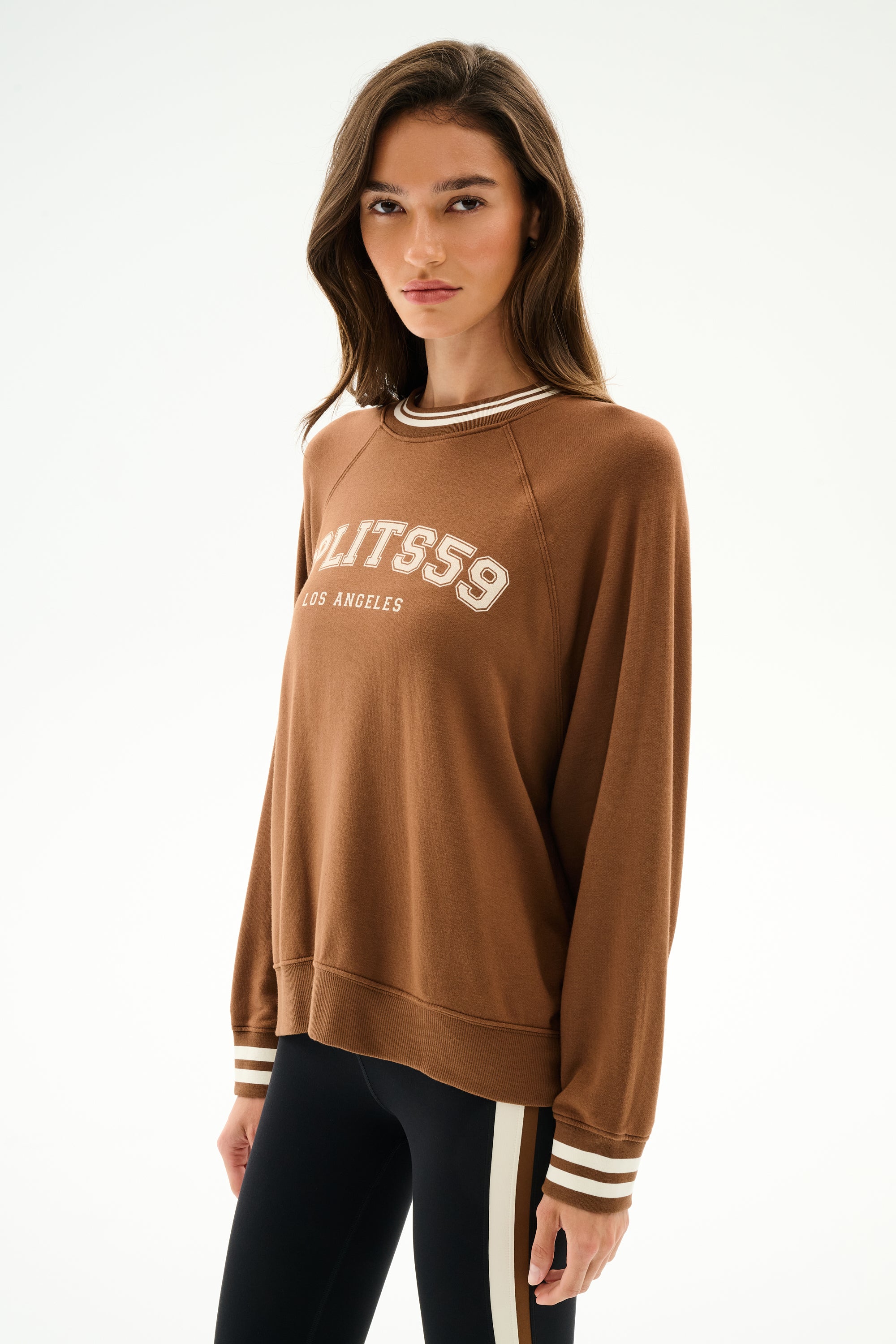Woman wearing the Andie Oversized Fleece Varsity Stripe Sweatshirt - Toffee/Splits59 Los Angeles and black leggings with beige and white side stripes, standing against a plain white background.