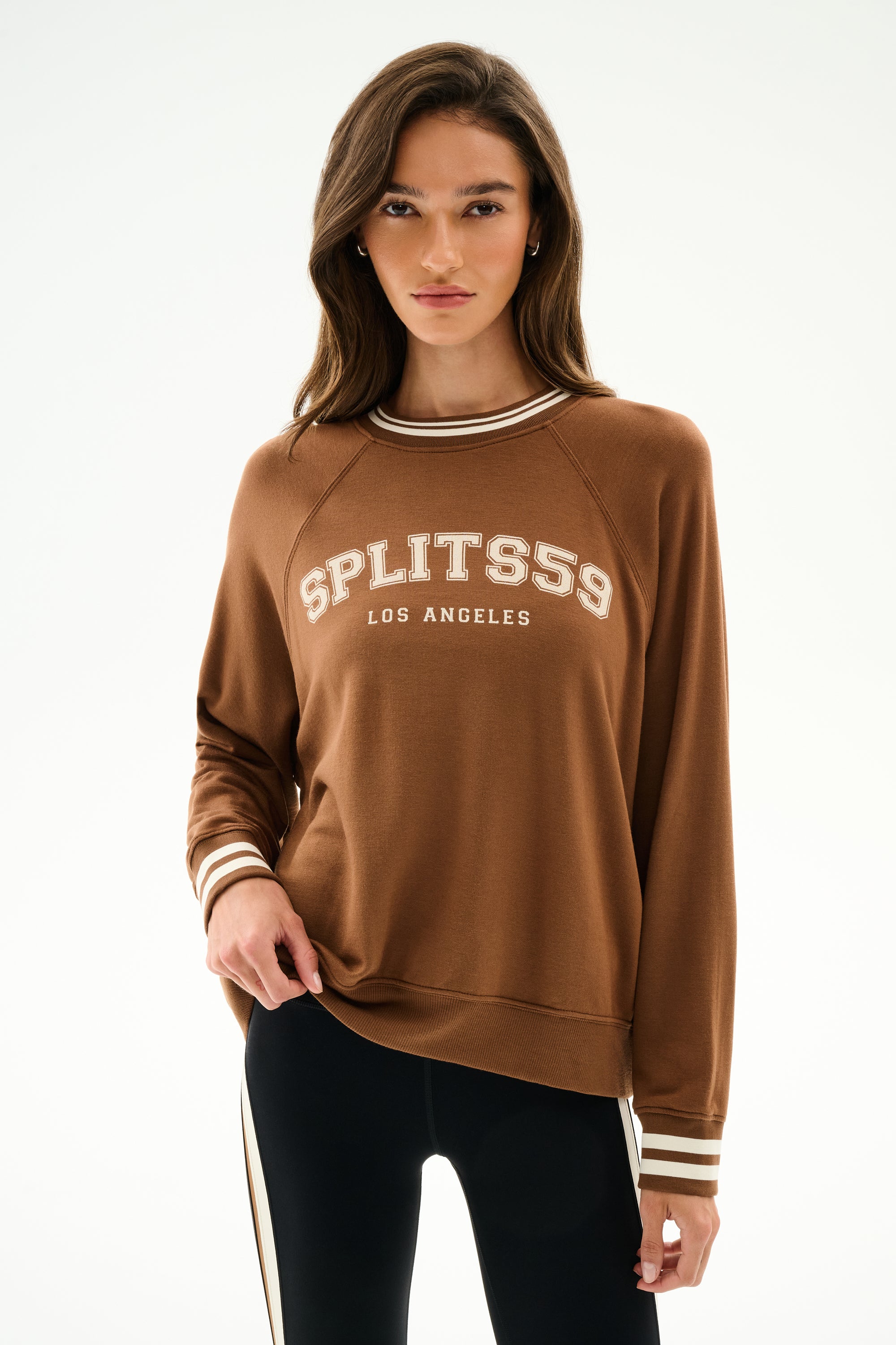 A person wears the Andie Oversized Fleece Varsity Stripe Sweatshirt - Toffee/Splits59 Los Angeles by SPLITS59 with black leggings against a plain white background.