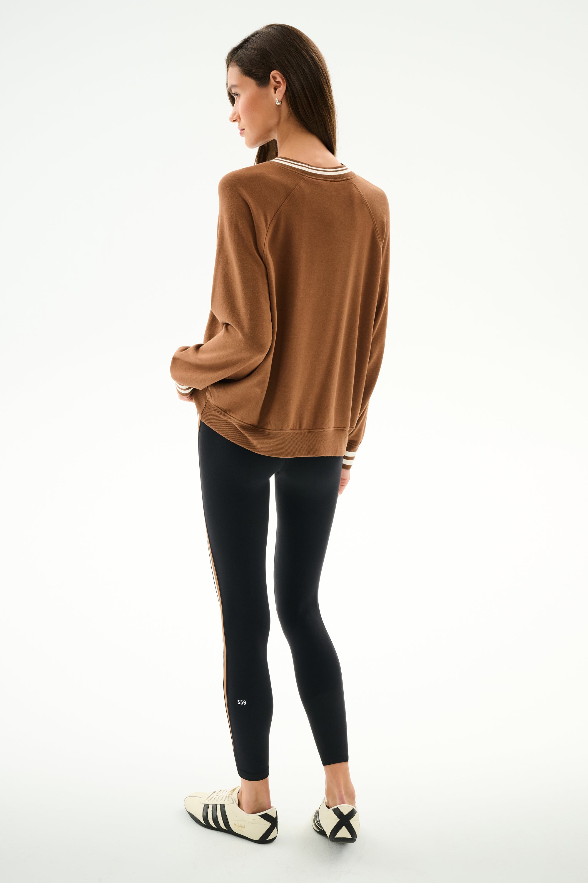 Person facing away, wearing the Andie Oversized Fleece Varsity Stripe Sweatshirt - Toffee/Splits59 Los Angeles, black spandex-blend stripe leggings, and white sneakers with black stripes.