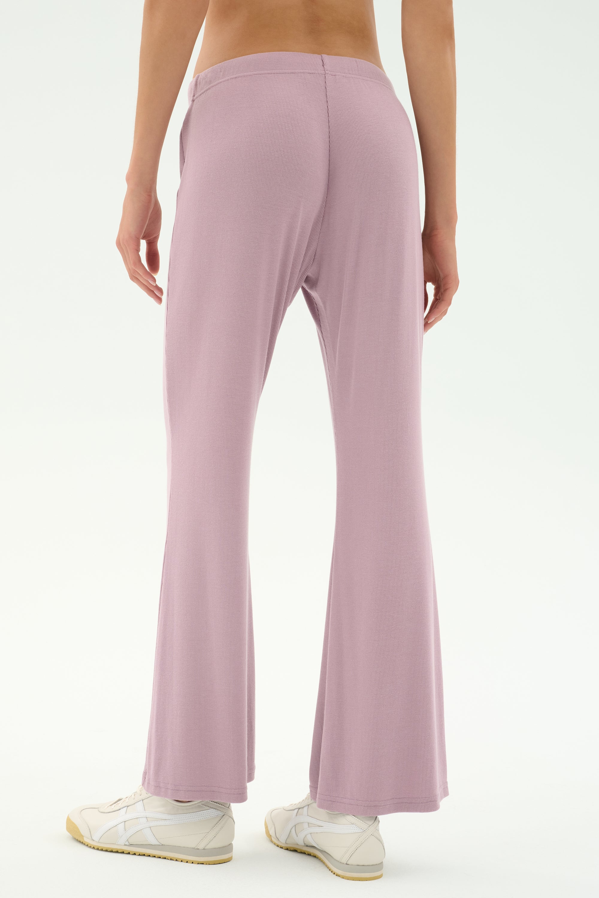 Model wears the SPLITS59 Blaire Rib Pant in Blush, showcasing the light purple flared silhouette made from soft modal-spandex, styled with white sneakers and photographed from behind against a plain backdrop.