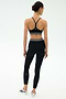 A woman faces away, wearing the SPLITS59 Cali Active Rib Bra in black with high-waisted leggings featuring white stripes and white sneakers, set against a plain light background.