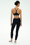 A woman faces away, wearing the SPLITS59 Cali Active Rib Bra in black with high-waisted leggings featuring white stripes and white sneakers, set against a plain light background.