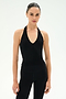 Wearing the SPLITS59 June Rib Halter in black, a person with dark hair pulled back poses against a plain white background, pairing the sleeveless halter top with black pants made from a soft modal blend fabric.