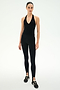 A woman stands against a white background, wearing the SPLITS59 June Rib Halter in black, styled with black spandex leggings and black sneakers with white stripes.