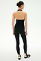 A person stands with their back to the camera, wearing the SPLITS59 June Rib Halter in black along with matching black leggings made from a soft modal blend, paired with black athletic shoes against a plain light background.