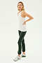A woman in a SPLITS59 Kiki Rib Tank Full Length - White, dark green leggings, and white sneakers stands against a plain background. She has one hand on her hip and her head tilted slightly, exuding the confidence of someone who enjoys running.