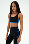 A woman wearing the SPLITS59 Maci Airweight Bra in Black/Classic Blue and coordinating nylon leggings with blue stripes, standing against a plain white background.