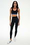 A woman wearing the SPLITS59 Maci Airweight Bra in Black/Classic Blue with matching black leggings featuring blue stripes, paired with white sneakers, stands against a plain white background.