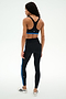 A person stands facing away against a plain white background, wearing the SPLITS59 Maci Airweight Bra in Black/Classic Blue.