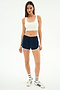 A woman faces forward in a white crop top, SPLITS59 Megan Woven Nylon Run Short in Indigo/Creme, striped socks, and white sneakers against a plain white background.