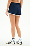 A person stands with their back to the camera, wearing SPLITS59 Megan Woven Nylon Run Short in Indigo/Creme, white socks with blue and red stripes, and white Adidas sneakers against a plain background.