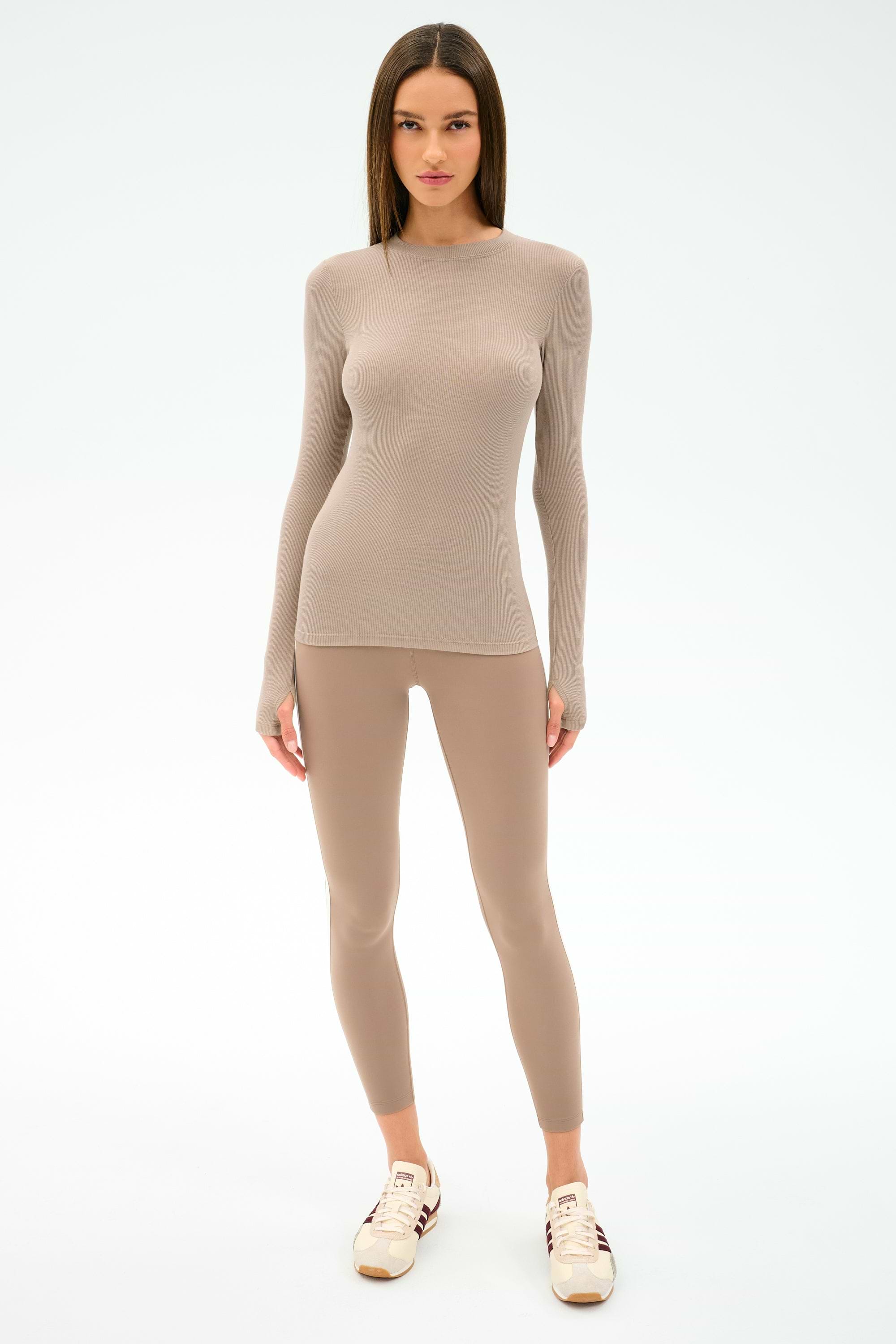 A woman faces forward in the SPLITS59 Louise Rib Long Sleeve - Latte and matching leggings—ideal beige-toned activewear for gym workouts—with white sneakers, set against a plain light background.
