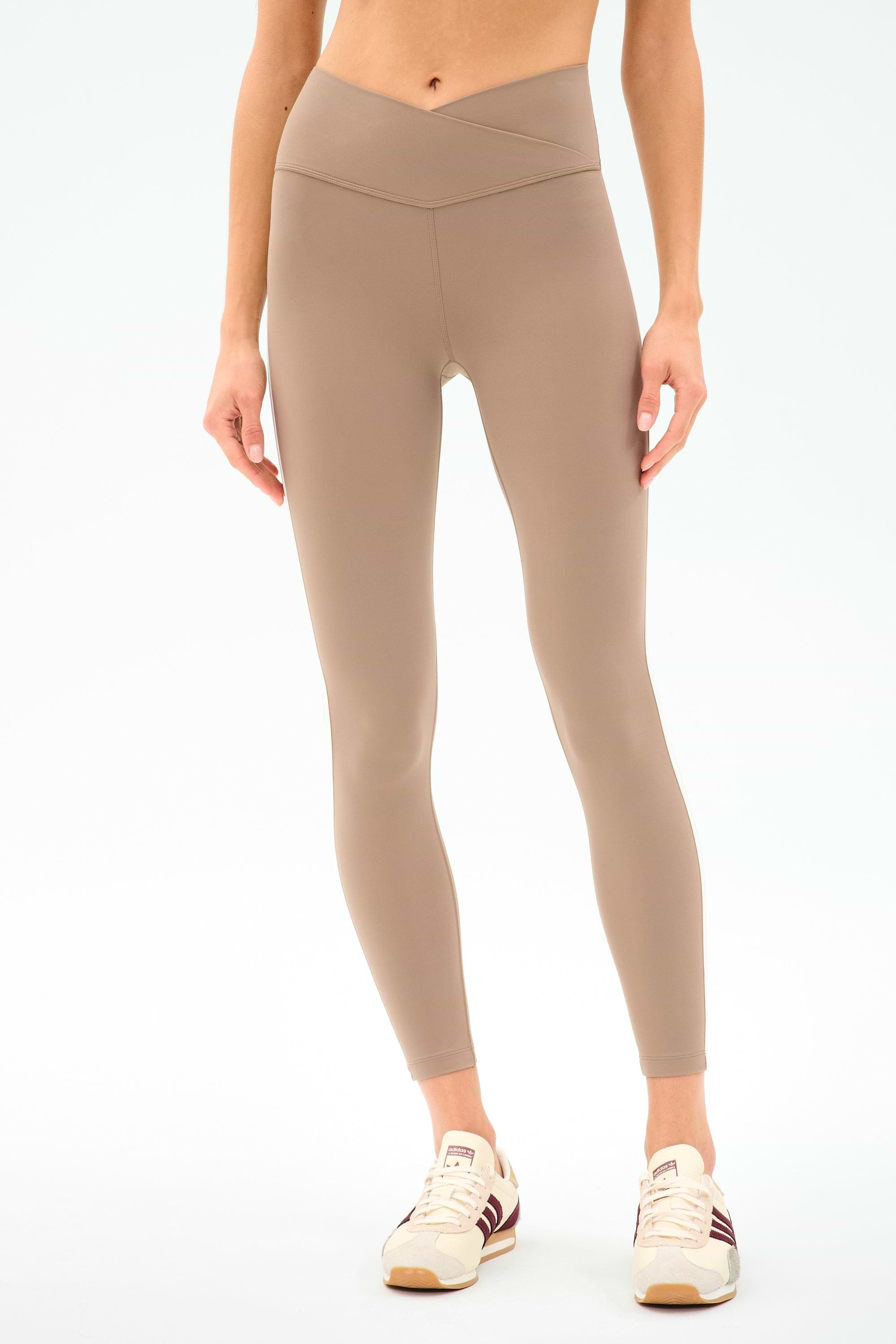 Someone wearing SPLITS59 Mia Rigor Legging w/ Stripe in Latte/White and cream athletic shoes stands against a plain white background.