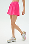 A person wearing the SPLITS59 Venus High Waist Rigor Skort in Berry and white athletic sneakers stands against a plain light background.