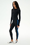 A woman is standing against a plain white background, dressed in the SPLITS59 Airweight Lite Long Sleeve Waist Length top in black, paired with black leggings featuring blue side stripes and white sneakers—an ideal outfit for gym workouts.