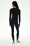 A person stands facing away, wearing the SPLITS59 Airweight Lite Long Sleeve Waist Length top in black and matching leggings with blue side stripes, paired with white sneakers against a plain light background—an ideal outfit for gym workouts.