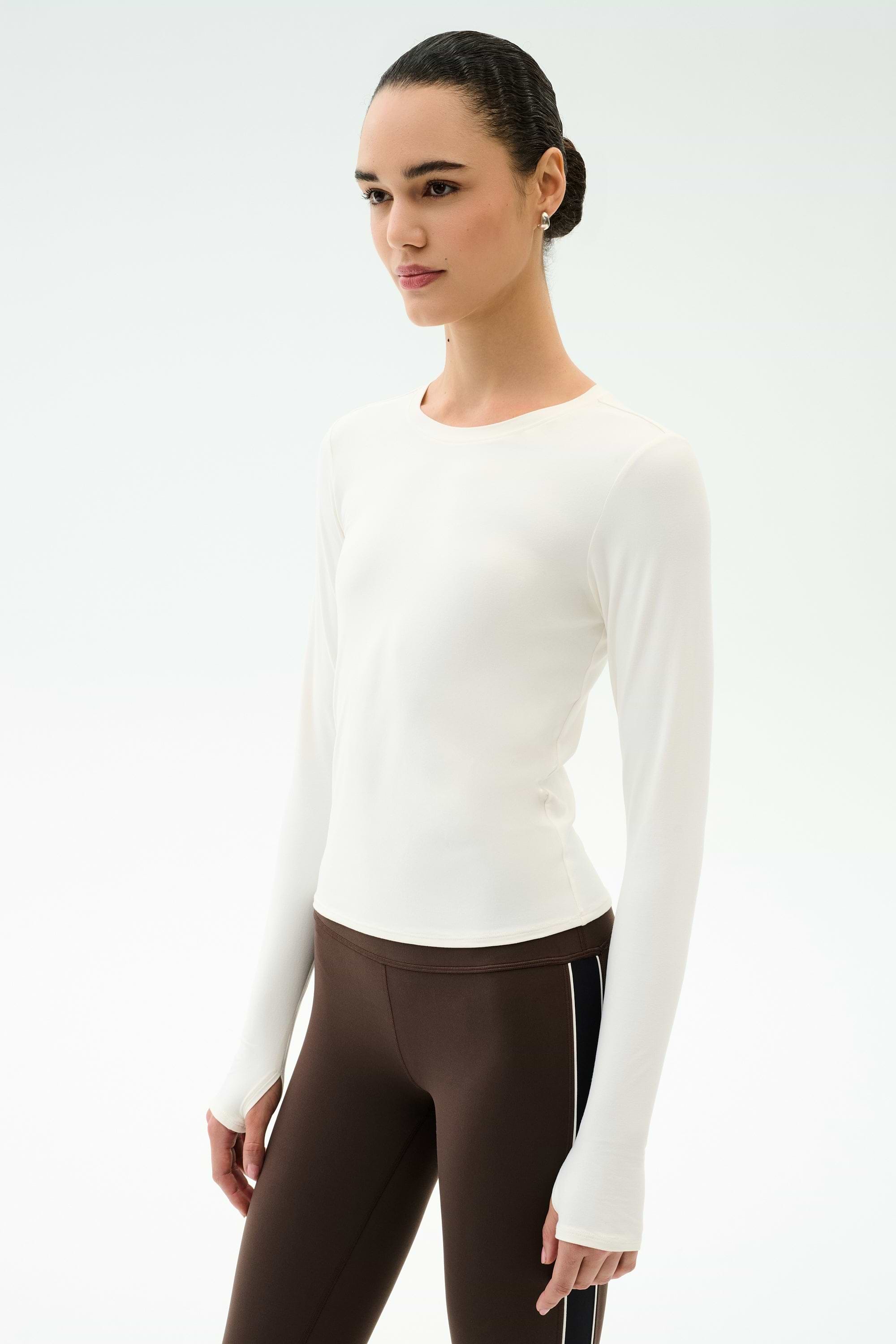 Wearing the SPLITS59 Airweight Lite Long Sleeve Waist Length in white and brown side-stripe leggings, a person stands against a light background—perfect for gym workouts.