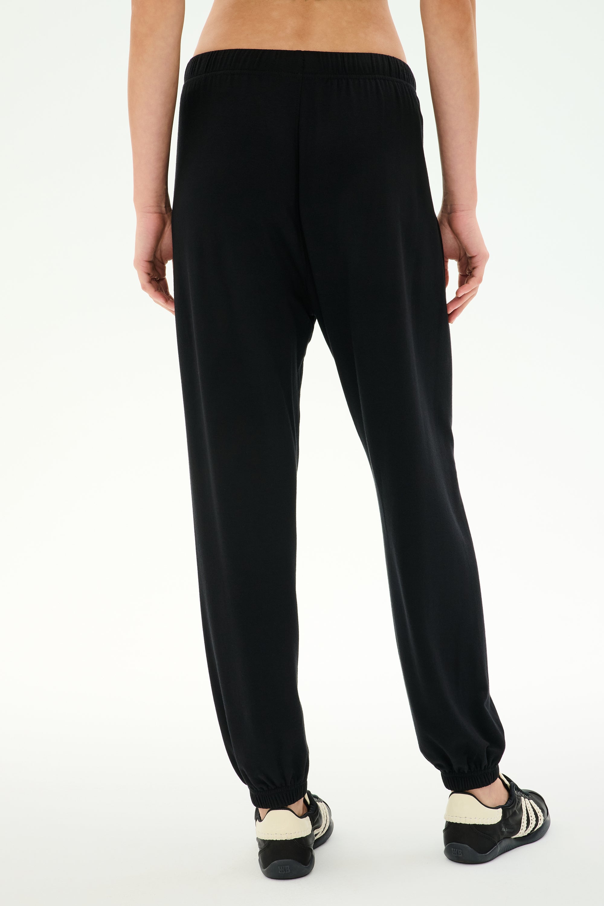 A person shown from the back against a plain white background wears the SPLITS59 Andie Oversized Fleece Sweatpant in black, paired with black-and-white sneakers—an ideal choice for cool weather workouts. Crafted with care in Los Angeles.