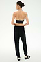 A person with hair in a bun wears a black halter top, SPLITS59 Andie Oversized Fleece Sweatpant in black, and black sneakers with white stripes, standing against a plain white background and facing away—perfect for cool weather workouts.