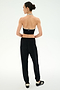 A person with hair in a bun wears a black halter top, SPLITS59 Andie Oversized Fleece Sweatpant in black, and black sneakers with white stripes, standing against a plain white background and facing away—perfect for cool weather workouts.