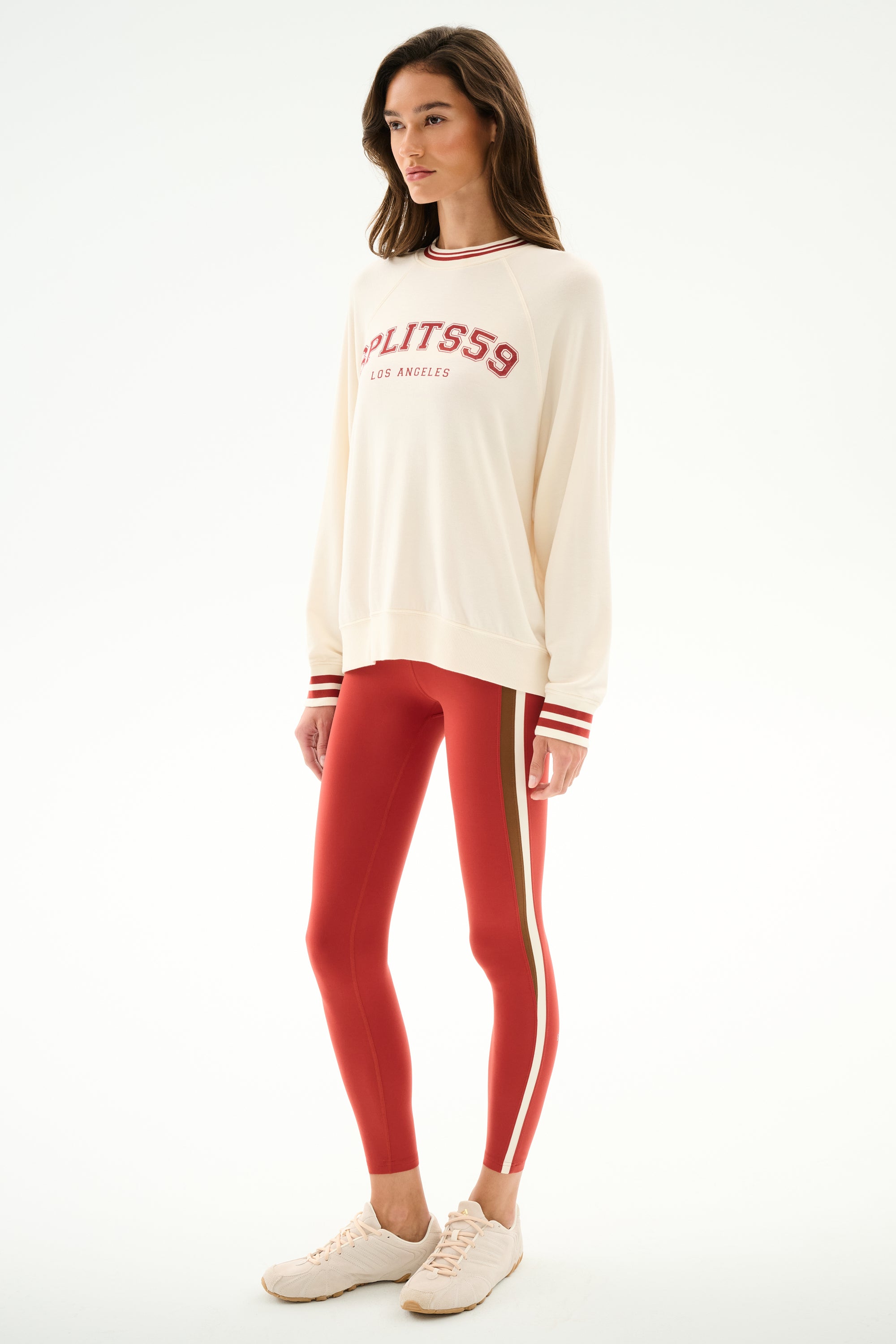 Woman in studio wears Andie Oversized Fleece Varsity Stripe Sweatshirt - Creme/Splits59 Los Angeles, red striped leggings, and beige sneakers by SPLITS59.