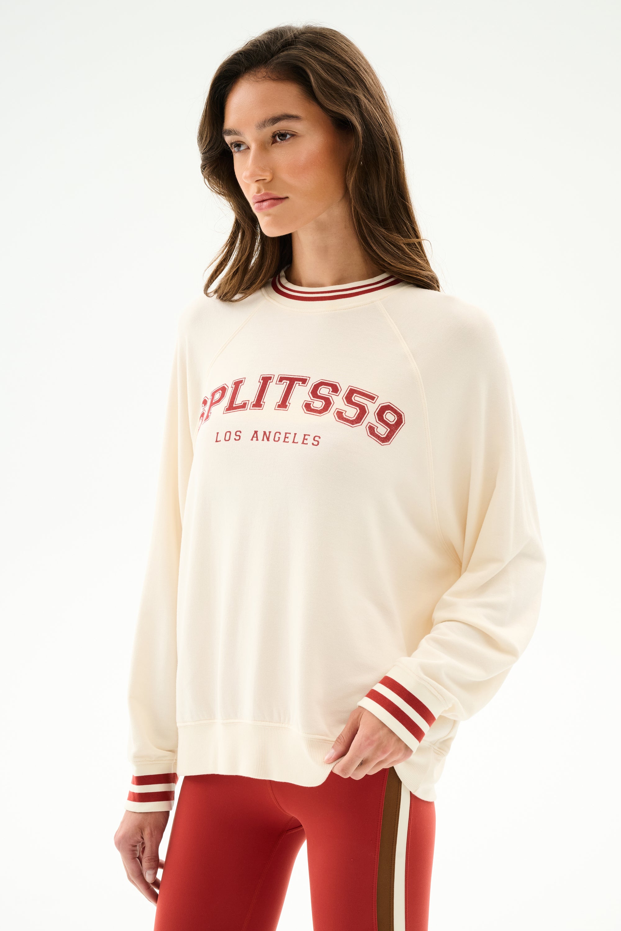 Woman wears the Andie Oversized Fleece Varsity Stripe Sweatshirt - Creme/Splits59 Los Angeles with red leggings featuring tan and white side stripes.