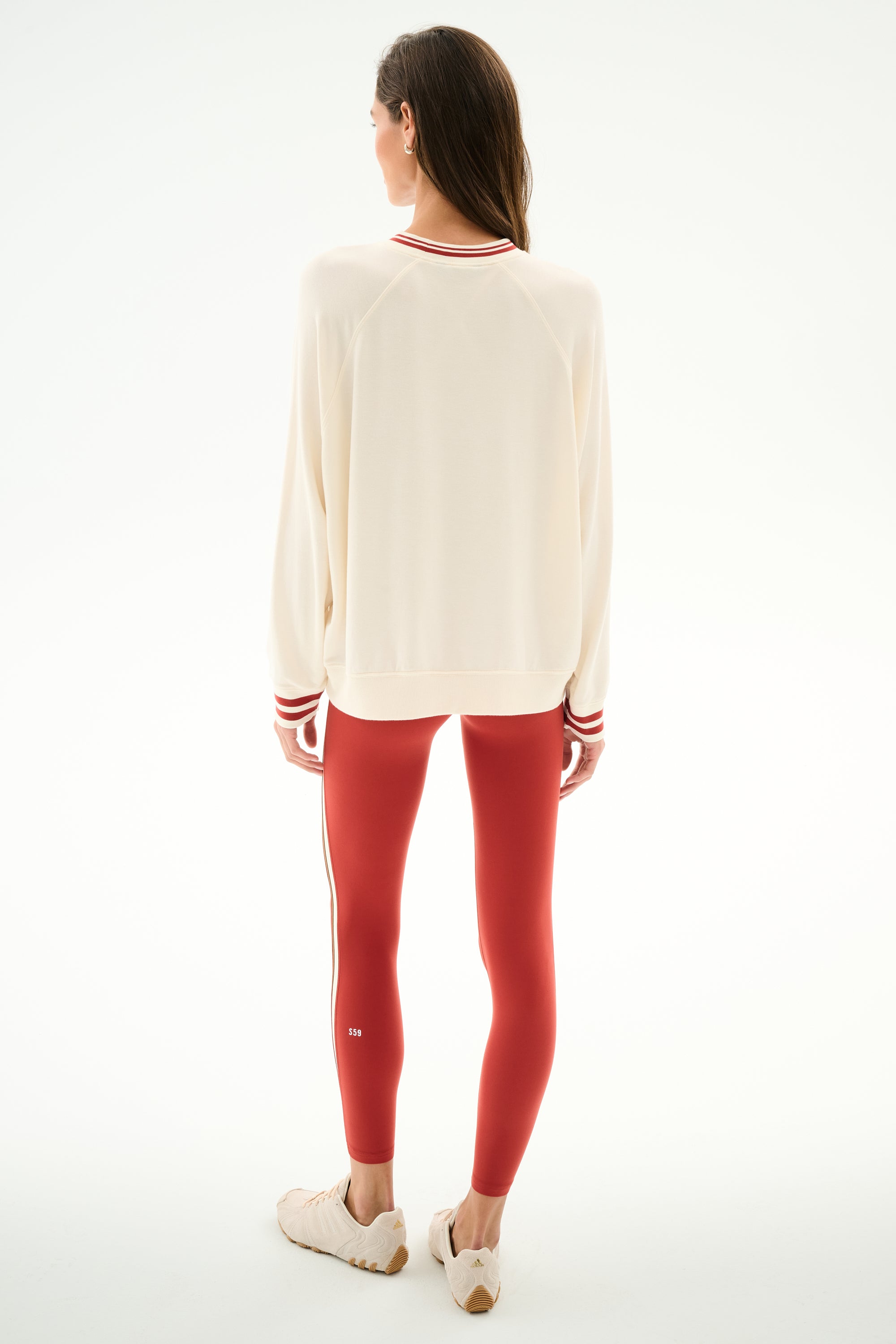 A woman faces away wearing the Andie Oversized Fleece Varsity Stripe Sweatshirt - Creme/Splits59 Los Angeles by SPLITS59, red leggings with white stripes, and light sneakers.