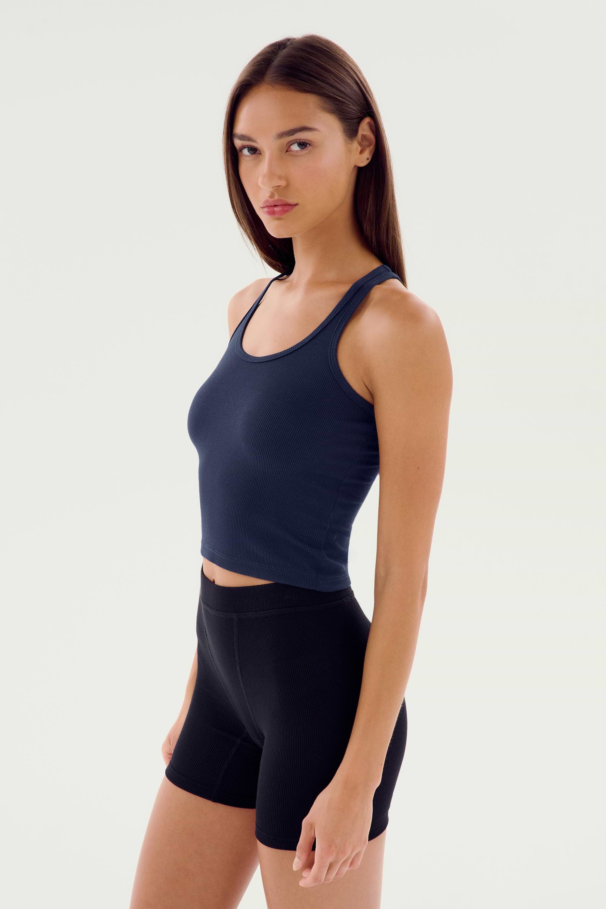 A person with long hair is wearing a navy SPLITS59 Ashby Rib Crop - Indigo and black shorts, standing against a plain white background.
