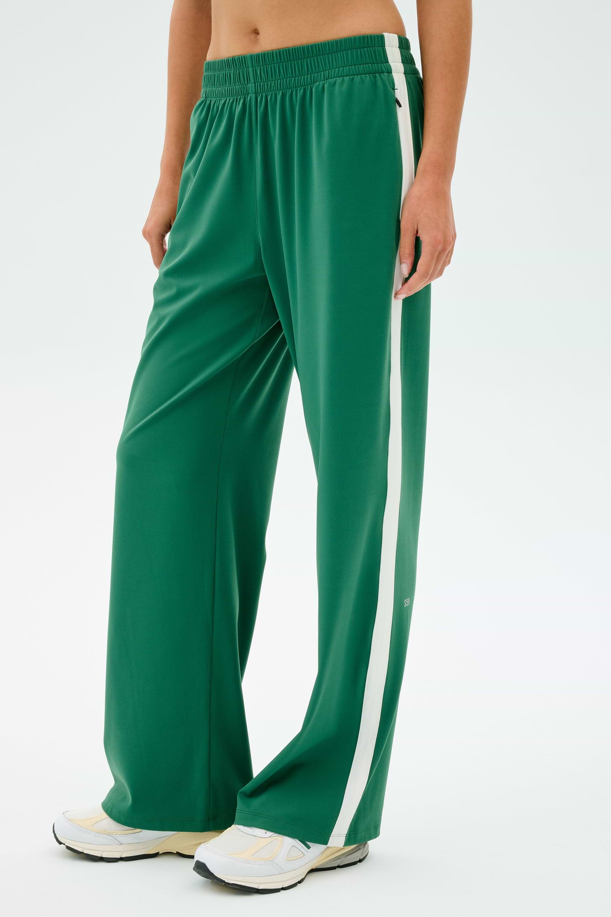 Someone in SPLITS59's Maxie Rigor Track Pant, featuring a white side stripe, paired with white sneakers stands against a plain background.