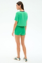 A woman faces away on a white background, wearing the SPLITS59 Djuna Crop Ringer in Spearmint/Indigo with matching green athletic shorts and white sneakers with green stripes. The cropped T-shirt is made from soft viscose with elastane for stretch.
