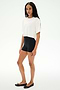 A person stands against a white background, wearing the SPLITS59 Djuna Oversized Crop Jersey Tee in white, paired with black fitted spandex shorts and black flats.