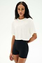 A person with long braided hair wears the SPLITS59 Djuna Oversized Crop Jersey Tee in white and fitted black spandex-blend shorts, standing against a plain white background.