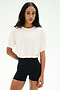 A woman faces forward against a white background, wearing the SPLITS59 Djuna Oversized Crop Jersey Tee in white paired with high-waisted black stretchy shorts.