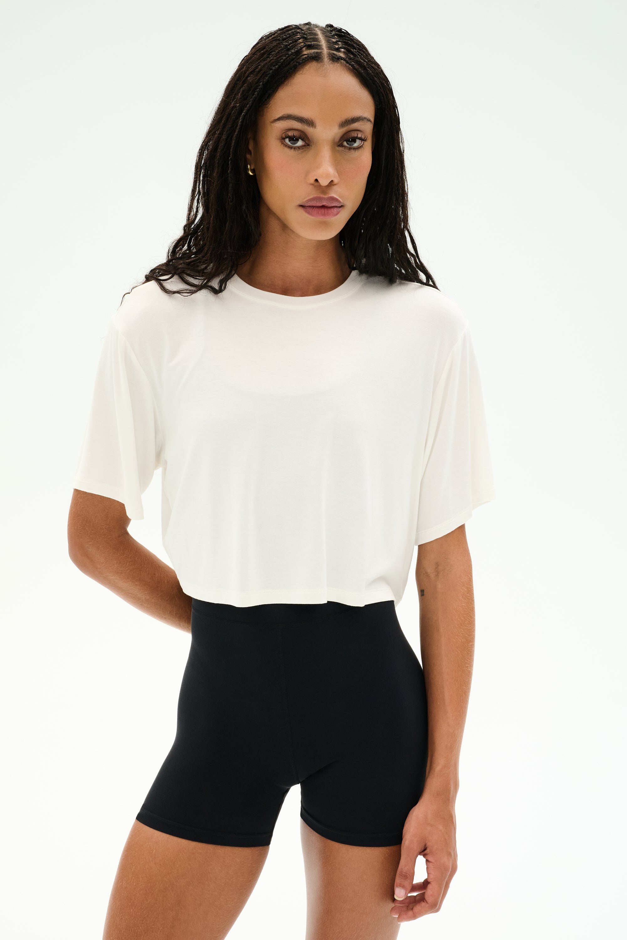 A woman faces forward against a white background, wearing the SPLITS59 Djuna Oversized Crop Jersey Tee in white paired with high-waisted black stretchy shorts.