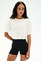 A woman faces forward against a white background, wearing the SPLITS59 Djuna Oversized Crop Jersey Tee in white paired with high-waisted black stretchy shorts.