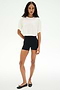 A person stands against a plain white background wearing the SPLITS59 Djuna Oversized Crop Jersey Tee in white, paired with black shorts and black ballet flats.