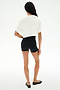 A person stands on a white background, facing away, wearing the SPLITS59 Djuna Oversized Crop Jersey Tee in white, paired with black spandex shorts and black flats.