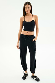A woman stands against a white background wearing a black tank top, black SPLITS59 Nico Airweight Cargo Pant for lightweight comfort, and black sneakers with white stripes.
