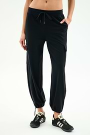 A person wears SPLITS59 Nico Airweight Cargo Pant in black for lightweight comfort, paired with black athletic shoes, standing against a plain light background.