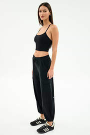 A woman poses against a plain background in the SPLITS59 Nico Airweight Cargo Pant in black, paired with a black crop top and black sneakers with white stripes.