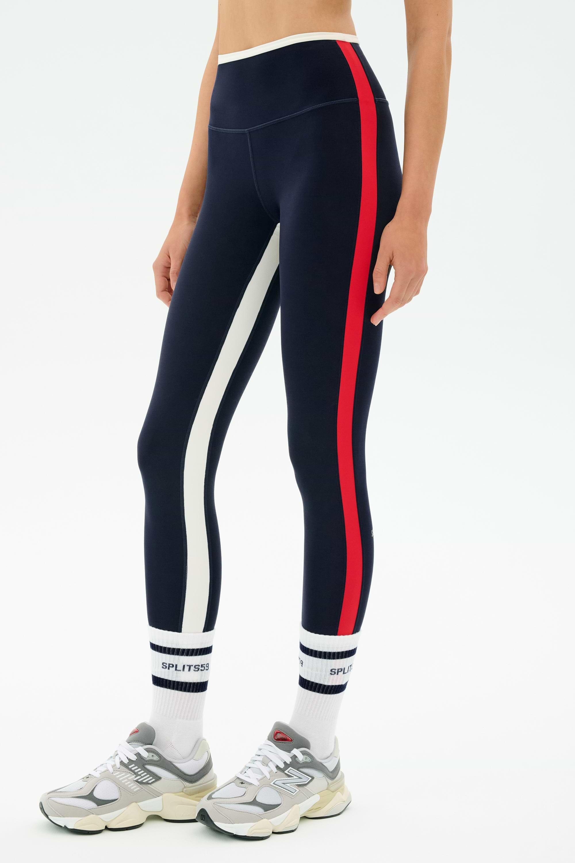 A person wearing SPLITS59 Sam High Waist Rigor 7/8 leggings in Indigo/White, white logo socks, and gray sneakers is shown from midriff to feet against a white background.