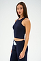 Wearing the Kiki Rib Crop Tank in Indigo by SPLITS59 and matching pants, a person stands against a plain background, looking forward.