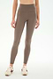 A person wearing SPLITS59′s Airweight High Waist 7/8 Pocket Legging in Lentil, paired with cream sneakers featuring brown accents, stands against a plain white background.