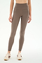A person wearing SPLITS59′s Airweight High Waist 7/8 Pocket Legging in Lentil, paired with cream sneakers featuring brown accents, stands against a plain white background.