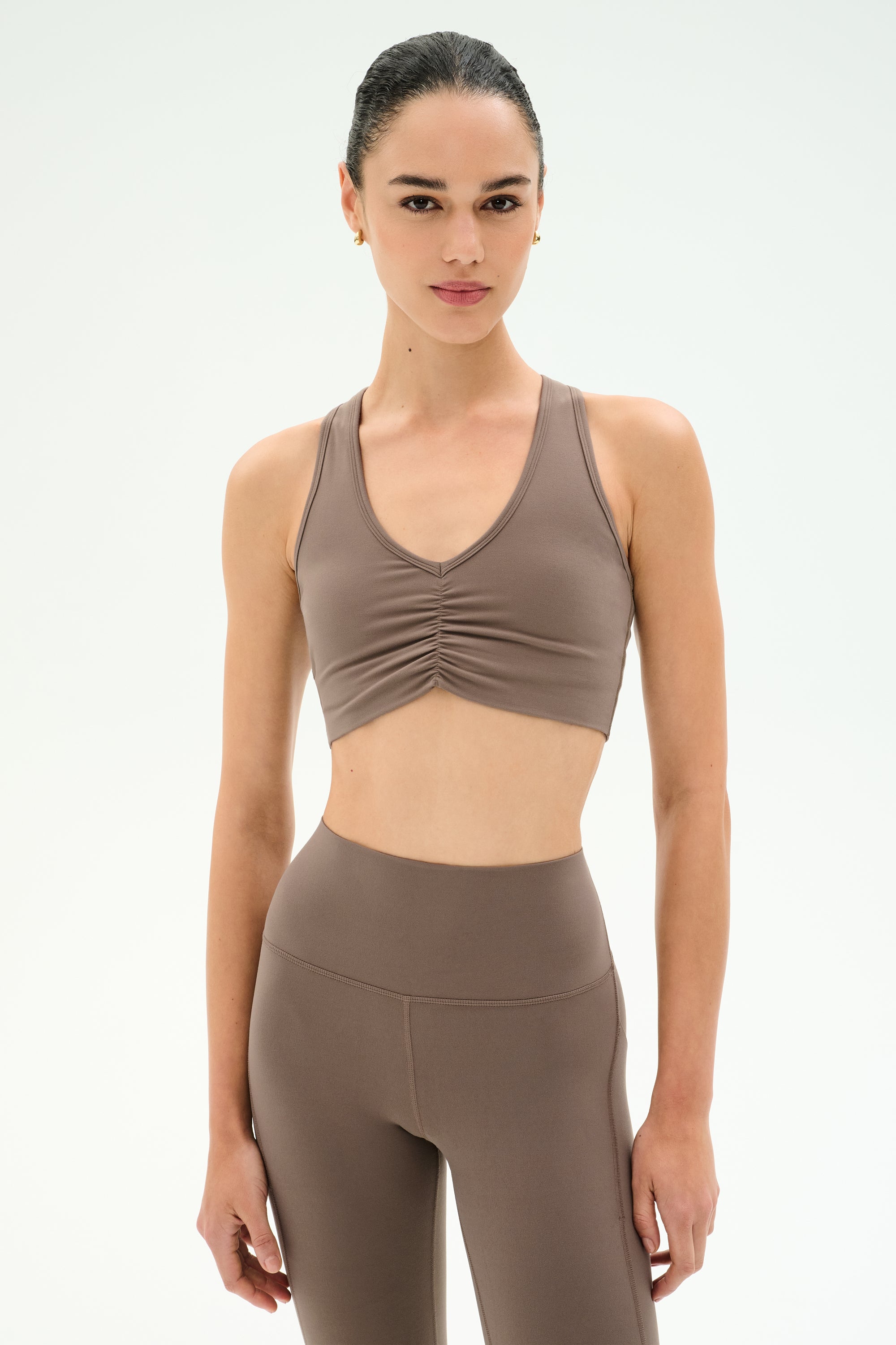 Woman wearing the SPLITS59 Airweight Bra With Ruching in Lentil and matching high-waisted leggings, standing against a plain light background.