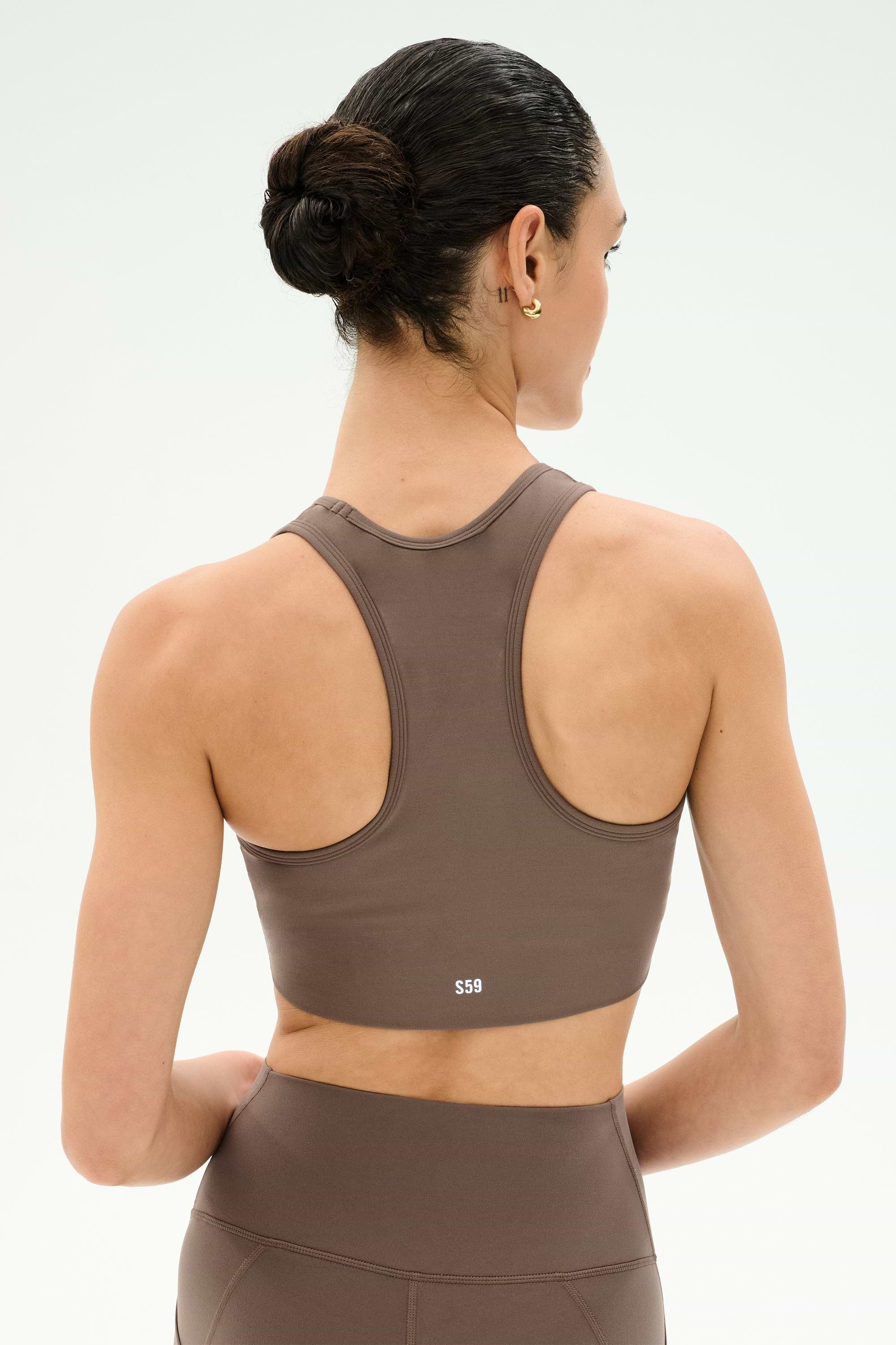 A person with dark hair in a bun is shown from the back, wearing the SPLITS59 Airweight Bra With Ruching in Lentil and matching leggings, both made from stretch fabric, against a plain light background.